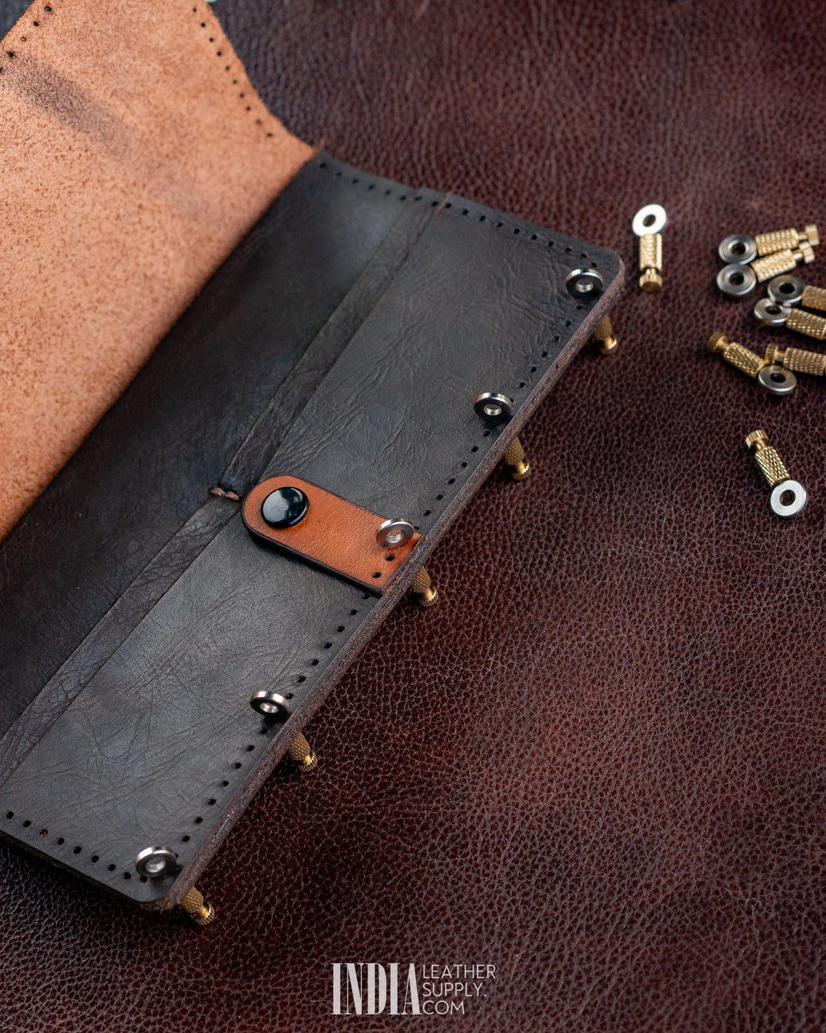 Positioning needles aligning layers of a black leather wallet before sewing