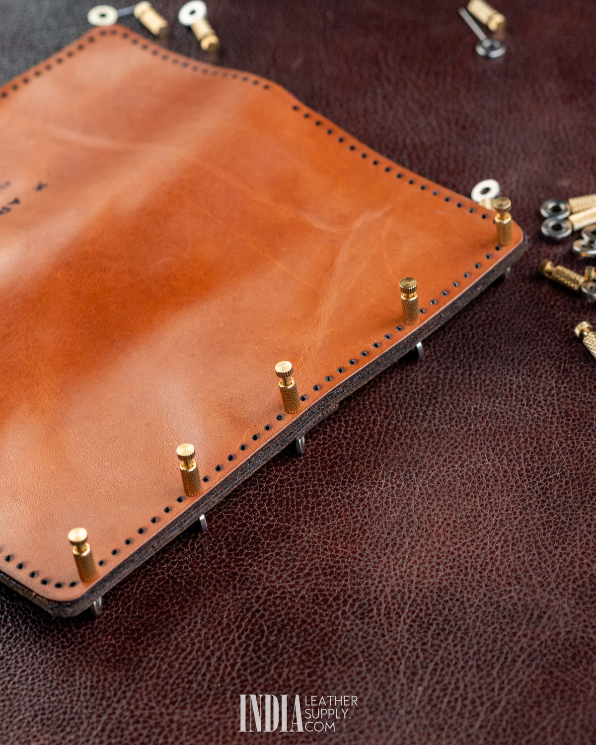 Brass positioning needles holding tan leather layers in place for stitching